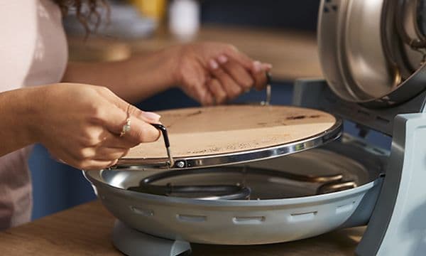 Hænder der lægger pizzasten ind i Kenwood My Pizzeria pizzaovn