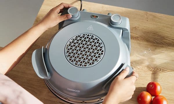 Lähikuvassa kädet, jotka parhaillaan avaavat Kenwood My Pizzeria -pitsauunin kantta