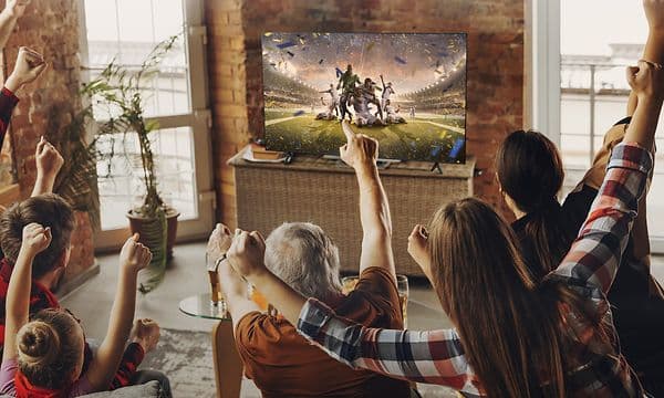 En familj sitter i en soffa och tittar på fotboll på en TCL MQLED75L-platt-TV.