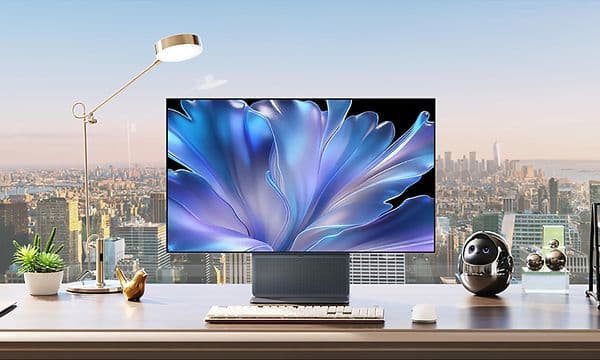 TCL 32X3A-skärm på ett skrivbord framför ett fönster med stadsutsikt, med ett blått blomliknande motiv på skärmen.