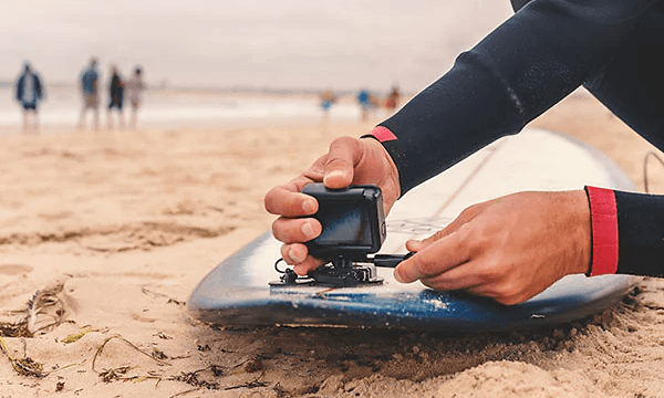 person monterer actionkamera på surfebrett på strand