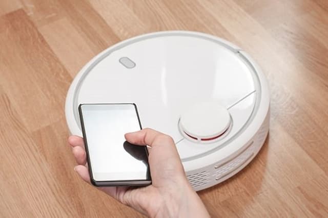 Någon styr en vit robotdammsugare från sin mobiltelefon.