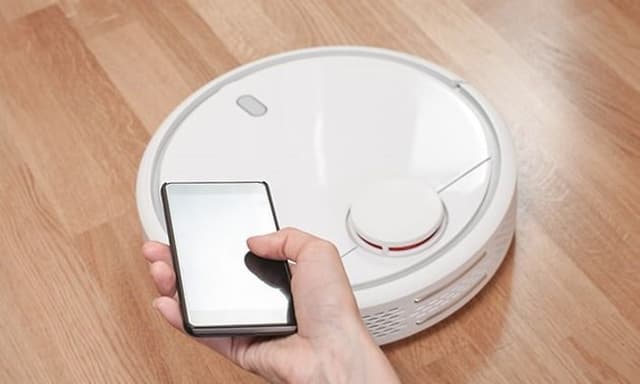 Någon styr en vit robotdammsugare från sin mobiltelefon.