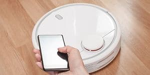 Någon styr en vit robotdammsugare från sin mobiltelefon.