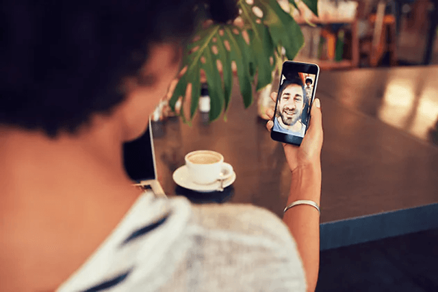 kvinne på kafé snakker i videosamtale med mann på smarttelefon 