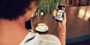 kvinne på kafé snakker i videosamtale med mann på smarttelefon 