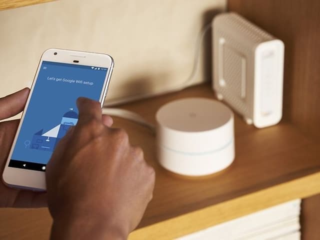 Två händer håller i en telefon med Google WiFi-installation på skärmen.