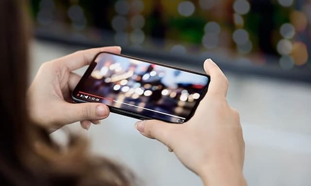 Person holder smarttelefon med begge hender og ser på film