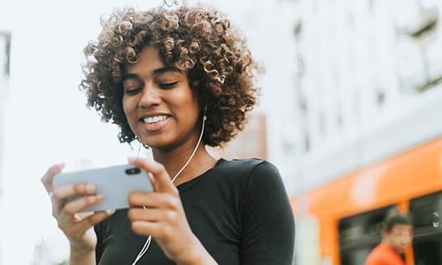 Jente ser på smarttelefon med ørepropper i ørene