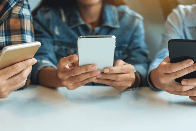 Tre unga personer sitter med sina smartphones i händerna.