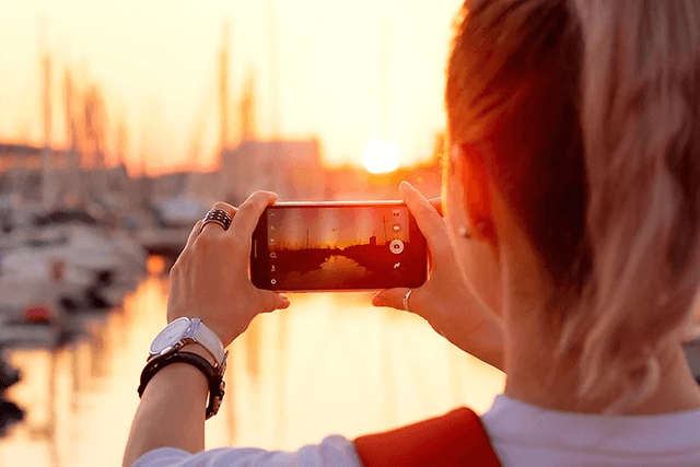 Kvinde der tager billede af en solnedgang ved en havn