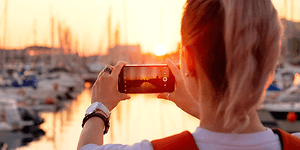 Kvinde der tager billede af en solnedgang ved en havn