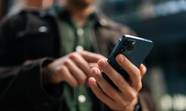 Man håller två olika mobiltelefoner i händerna, en iphone och en android, en vit och en svart. 