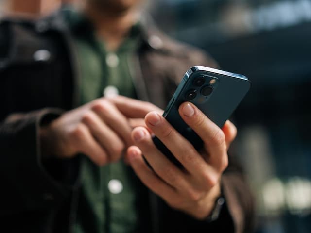 Man håller två olika mobiltelefoner i händerna, en iphone och en android, en vit och en svart.