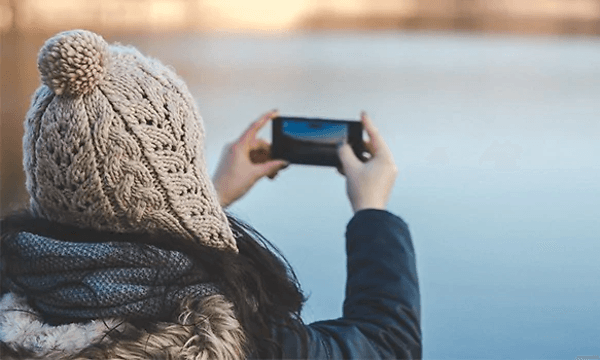 kvinne med lue og vinterjakke fotograferer med smarttelefon