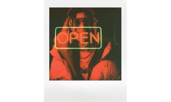 Et Polaroid-billede med en mand klædt i rødt og en dobbelteksponering af et neonskilt med teksten OPEN 