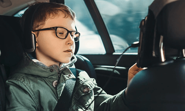 Poika istuu auton takapenkillä käyttäen etuistuimen takaosaan kiinnitettyä tablettia