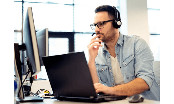 En man med headset och mikrofon sitter vid ett skrivbord med flera datorskärmar framför sig. 