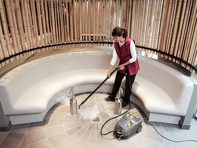 Kvinna som städar ett stengolv med en ångtvätt från Kärcher, ser ut som ett Spa eller badhus.