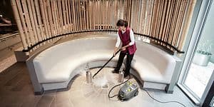 Kvinna som städar ett stengolv med en ångtvätt från Kärcher, ser ut som ett Spa eller badhus. 