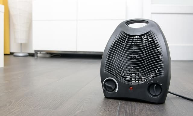Musta lämpöpuhallin lattialla valkoisen lipaston edessä