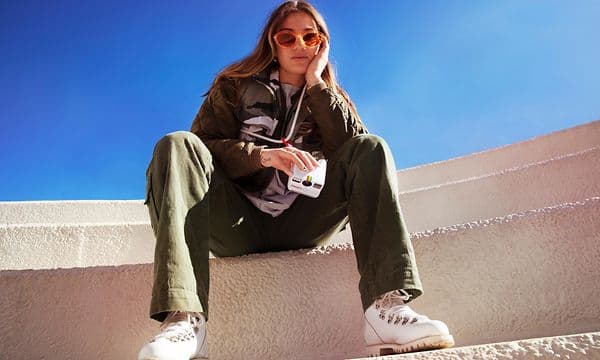 Portaissa istuva aurinkolasinen nainen pitelee Polaroid Go-kameraa