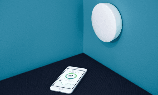 smarttelefon ligger ved siden av en veggmontert Airthings Wave Plus