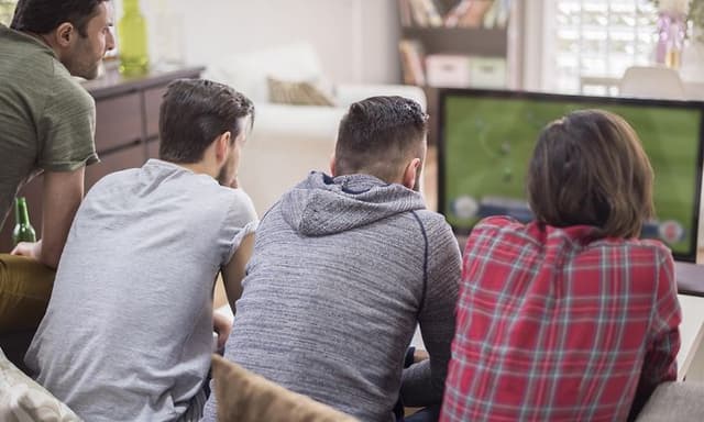 4 mænd i en sofa der ser TV