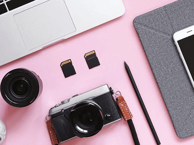 Photo equipment and mac and iphone laying on a pink table